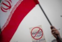 Seorang jamaah mengibarkan bendera Iran di depan plakat anti-Holocaust saat menghadiri protes atas pembakaran Al-Qu'ran setelah upacara Salat Jumat Teheran di masjid Agung Imam Khomeini, 27 Januari 2023. (Foto oleh Morteza Nikoubaz)