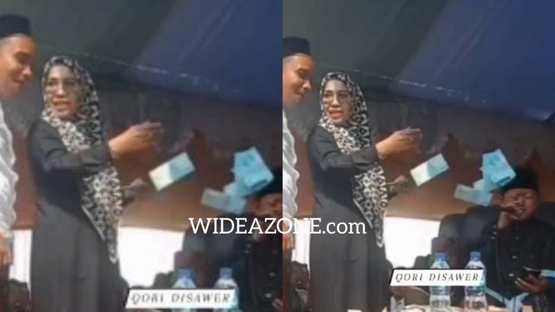 Seorang perempuan bersama pria naik ke panggung seraya memegang uang dan dengan santai melempar uang ke wajah qori cilik.